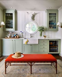 a kitchen with green cabinets and a red bench