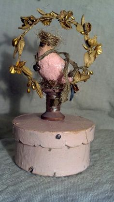 a pink and gold doll sitting on top of a wooden box with leaves around it