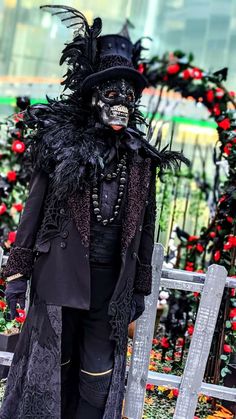 a man dressed in black and wearing a top hat with feathers on his head standing next to a fence