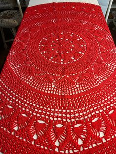 a red crocheted tablecloth on a bed with two chairs in the background