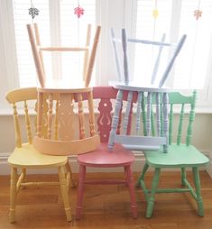 four different colored chairs sitting next to each other in front of a window with white shutters