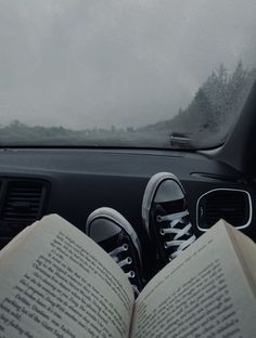 someone is reading a book while sitting in the passenger seat of a car on a rainy day