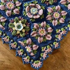 a blue crocheted doily with flowers on it sitting on a wooden floor