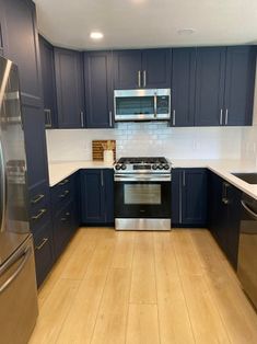 an empty kitchen with blue cabinets and stainless steel appliances in the center, along with wood flooring