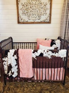 a baby crib with pink, brown and white bedding in front of a painting on the wall