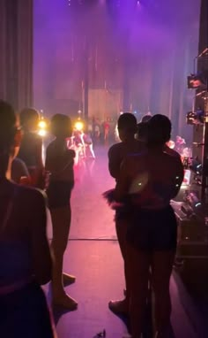 several people standing in front of a stage with bright lights on the walls and floor