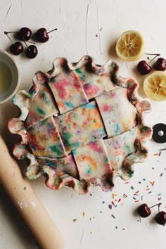 the pie is decorated with colorful icing and sprinkles next to some cherries