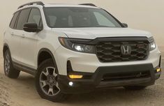 the front end of a white honda passport parked on top of a dirt hill with fog in the background