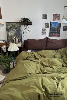 an unmade bed in a room with pictures on the wall and lamp next to it