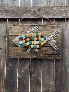 a fish made out of beads is hanging on a wooden fence with a string attached to it