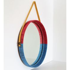 a mirror hanging on the wall with a leather strap around it's neck and an orange, blue, and red frame