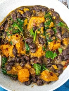 a white bowl filled with black beans and greens on top of a blue table cloth