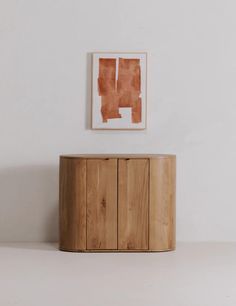 a wooden cabinet sitting in front of a painting on the wall next to a white wall