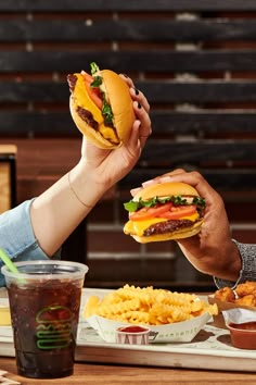 two people are holding up sandwiches and french fries to each other at a table with condiments