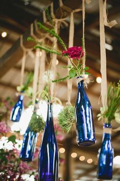 several blue vases with flowers hanging from the ceiling in a room filled with lights