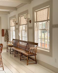 a wooden bench sitting in the middle of a living room next to two large windows