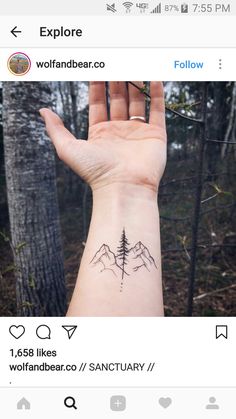 a person's hand with a small tattoo on the wrist and mountains in the background