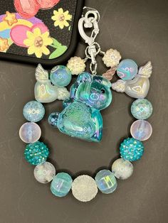 a necklace with glass beads and charms on it next to a wallet case that is decorated with an image of a fish