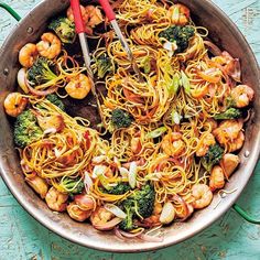 stir fry with shrimp, broccoli and noodles in a pan on a blue table