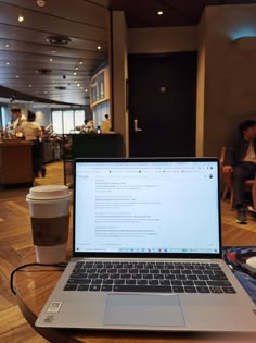 an open laptop computer sitting on top of a wooden table next to a cup of coffee