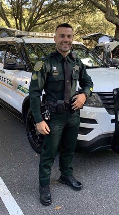 a police officer standing in front of his patrol car and smiling at the camera man