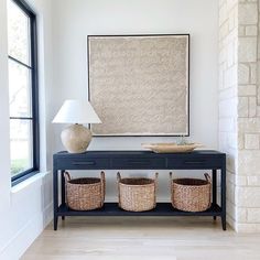 a table with two baskets and a lamp in front of a painting on the wall