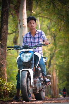 a man riding on the back of a motorcycle down a dirt road next to trees