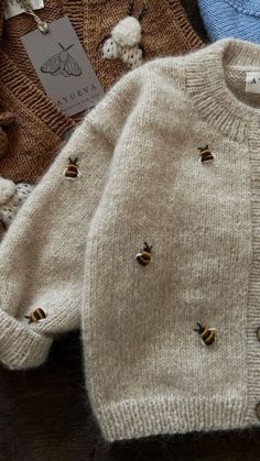 three sweaters with bees on them sitting next to each other in front of a tag