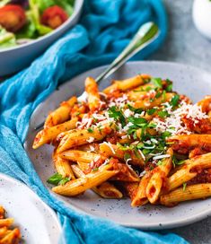 pasta with sauce and parmesan cheese on a white plate next to a bowl of salad