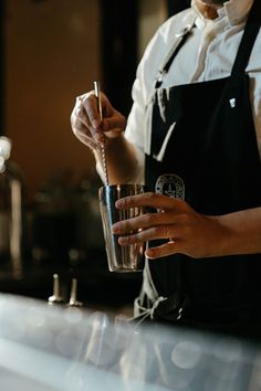 a person in an apron is holding a glass with a drink on it and stirring the liquid