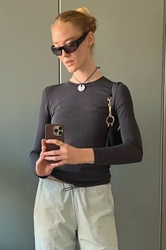 a woman standing in front of a mirror looking at her cell phone while wearing sunglasses