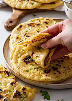 a hand holding a tortilla over a plate with some pita bread on it