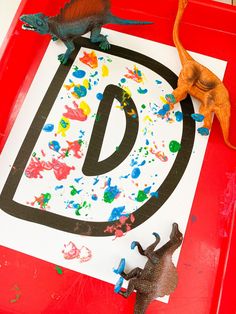 two toy dinosaurs are standing in front of a letter d sign