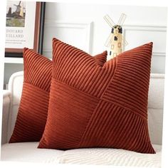 two orange pillows sitting on top of a white couch next to a framed photo and windmill