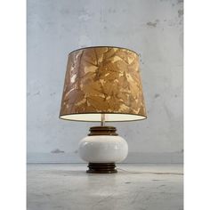 a lamp that is sitting on top of a table next to a white vase with a brown and gold shade