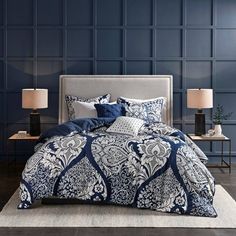 a bed with blue and white comforters in a room next to two lamps on tables