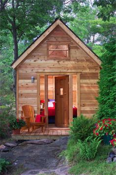 a small wooden cabin in the woods surrounded by greenery and trees with an open door