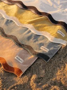 three towels are laying on the sand in different colors and patterns, one has a tag