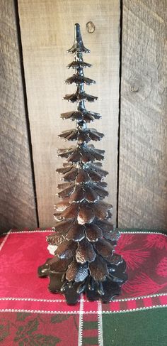 a small metal christmas tree sitting on top of a red and green table cloth next to a wooden wall