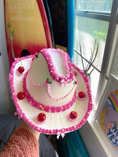 a hat made out of paper with cherries and beads on the top, sitting in front of a window