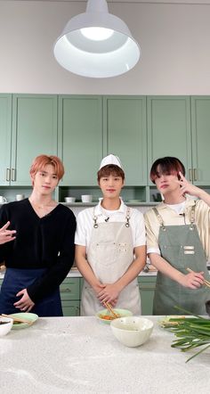 three young men standing next to each other in front of a kitchen counter with bowls and utensils on it