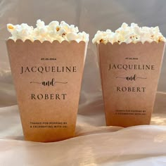 two brown paper cups filled with popcorn on top of a bed