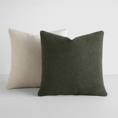 two pillows sitting next to each other on top of a white table with a black and green pillow