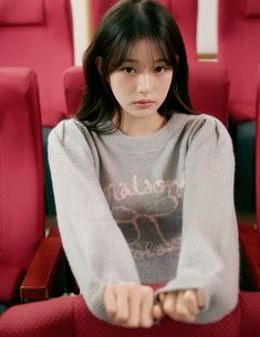 a young woman sitting in a red chair with her hand on the seat and looking at the camera