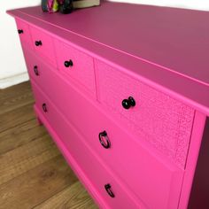 a pink dresser with black knobs on it's handles and drawers, in a room