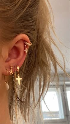 a close up of a person's ear wearing gold earrings with cross and arrow designs