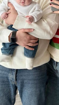 a man holding a baby in his arms while wearing a sweater and tie around his neck