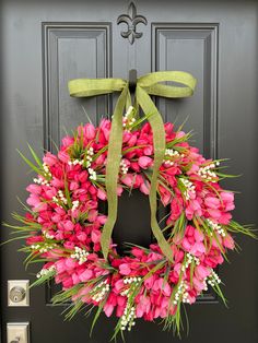 a wreath with pink flowers and green ribbon hanging on the front door to welcome guests