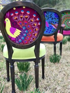 three colorful chairs sitting on top of a grass covered field