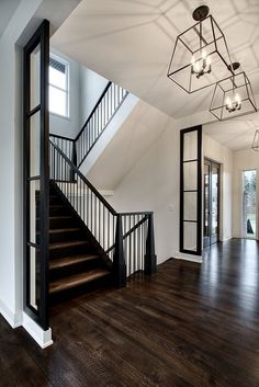 an empty room with wooden floors and black railings on the second floor is lit by two chandeliers